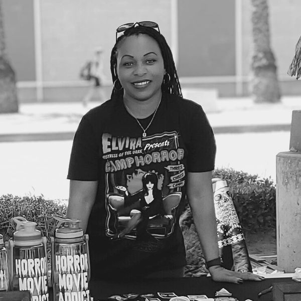 Woman at a table with horror-themed merchandise and a black Elvira Camp Horror t-shirt.