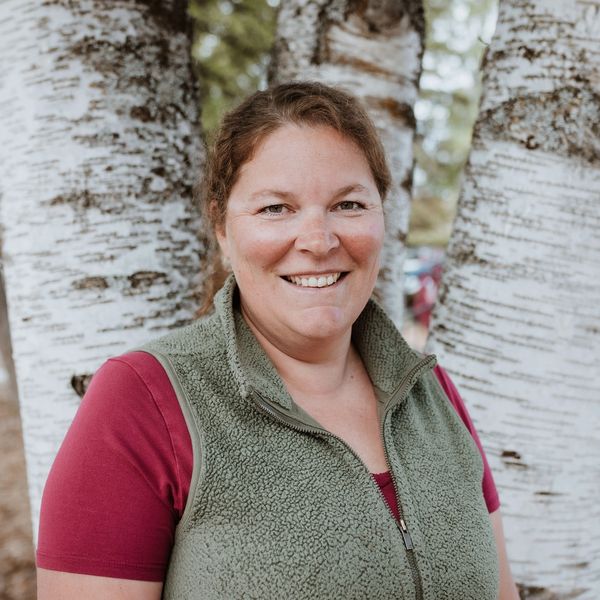 Smiling woman standing outdoors near white birch trees.
