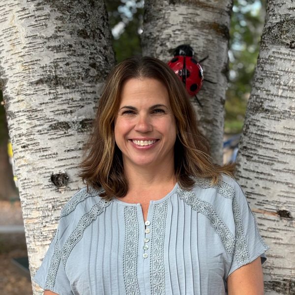 Smiling woman standing by birch trees outdoors.