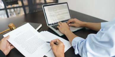 Two professionals reviewing and signing a contract with a laptop nearby.