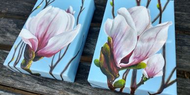 Two canvases with magnolia flower paintings on a wooden surface.