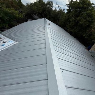 A newly installed silver metal roof on a building surrounded by trees.