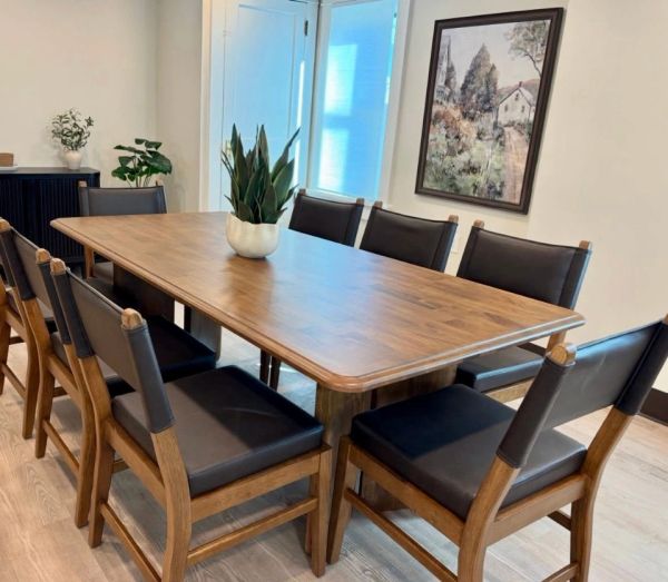 Wooden dining table with eight chairs and a plant centerpiece.