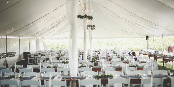 Large white tent with rows of white chairs and tables set for an event.