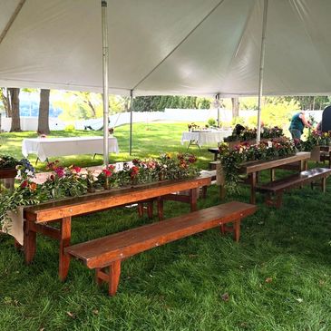 Wooden benches and floral decorations under a white tent on green grass.