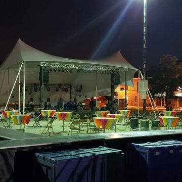 Outdoor event setup with stage, tables, and chairs at night.