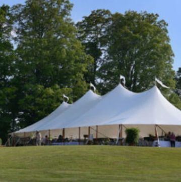 Large white event tent set up on green lawn with trees in background.