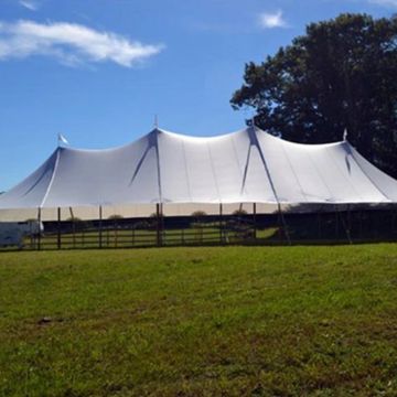 Large white event tent set up in a grassy field under a clear blue sky.