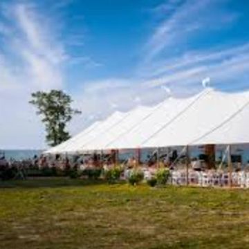 Large white event tent set up on a grassy area under a blue sky.