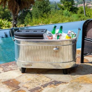 Metal cooler filled with ice and beverages beside a pool.