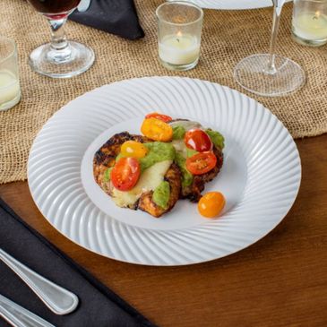 Grilled dish with cherry tomatoes and green sauce on a white plate.