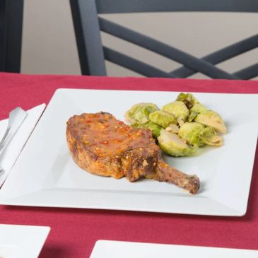Grilled pork chop with Brussels sprouts on a white square plate.