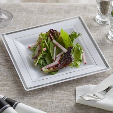 Fresh mixed green salad with radish slices on a white square plate.