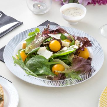 Fresh salad with greens, cherry tomatoes, and shaved cheese on a white plate.
