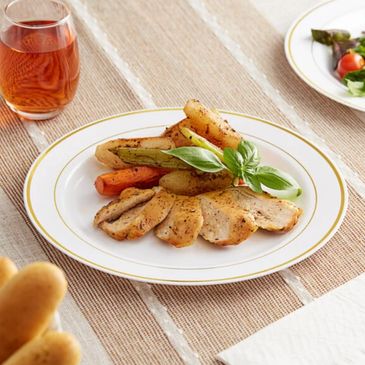 Grilled chicken with roasted vegetables and a basil garnish on a white plate.