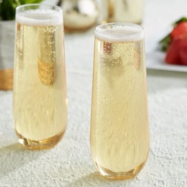 Two tall glasses filled with sparkling champagne on a textured white surface.