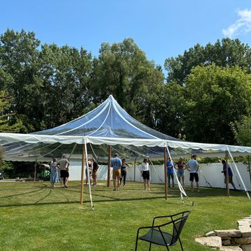 People setting up a large tent in a grassy backyard on a sunny day.