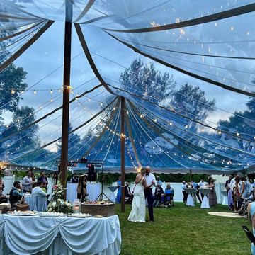 Bride and groom dancing under a transparent tent with string lights at an outdoor wedding.
