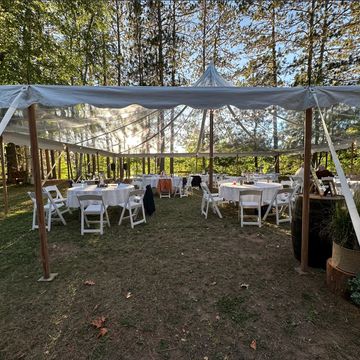 Outdoor event setup with tables and chairs under a white canopy tent.