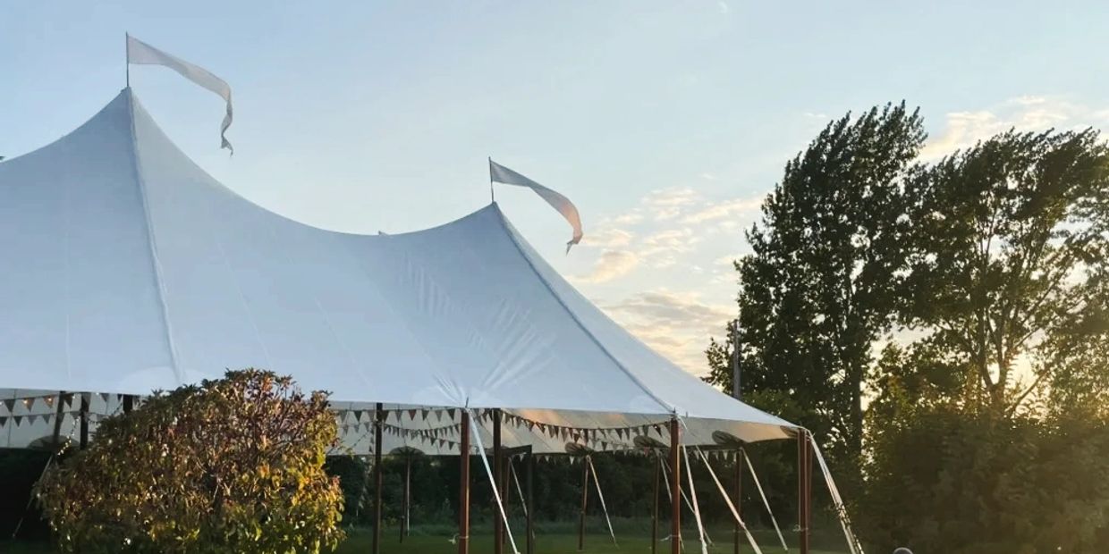 Large white event tent with flags set up outdoors at sunset.