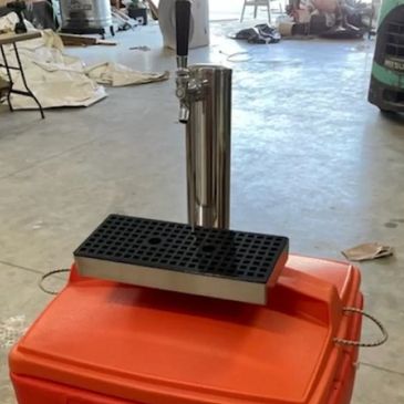 Portable beer tap setup on an orange cooler in a workshop.