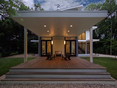 Modern house with a covered wooden deck in a wooded area.