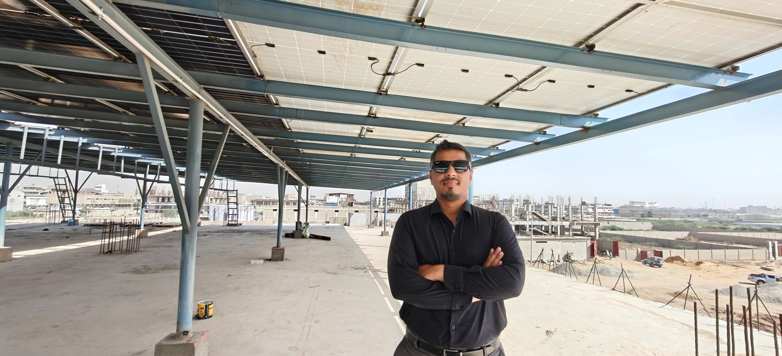 Man in sunglasses stands under solar panels at a construction site.