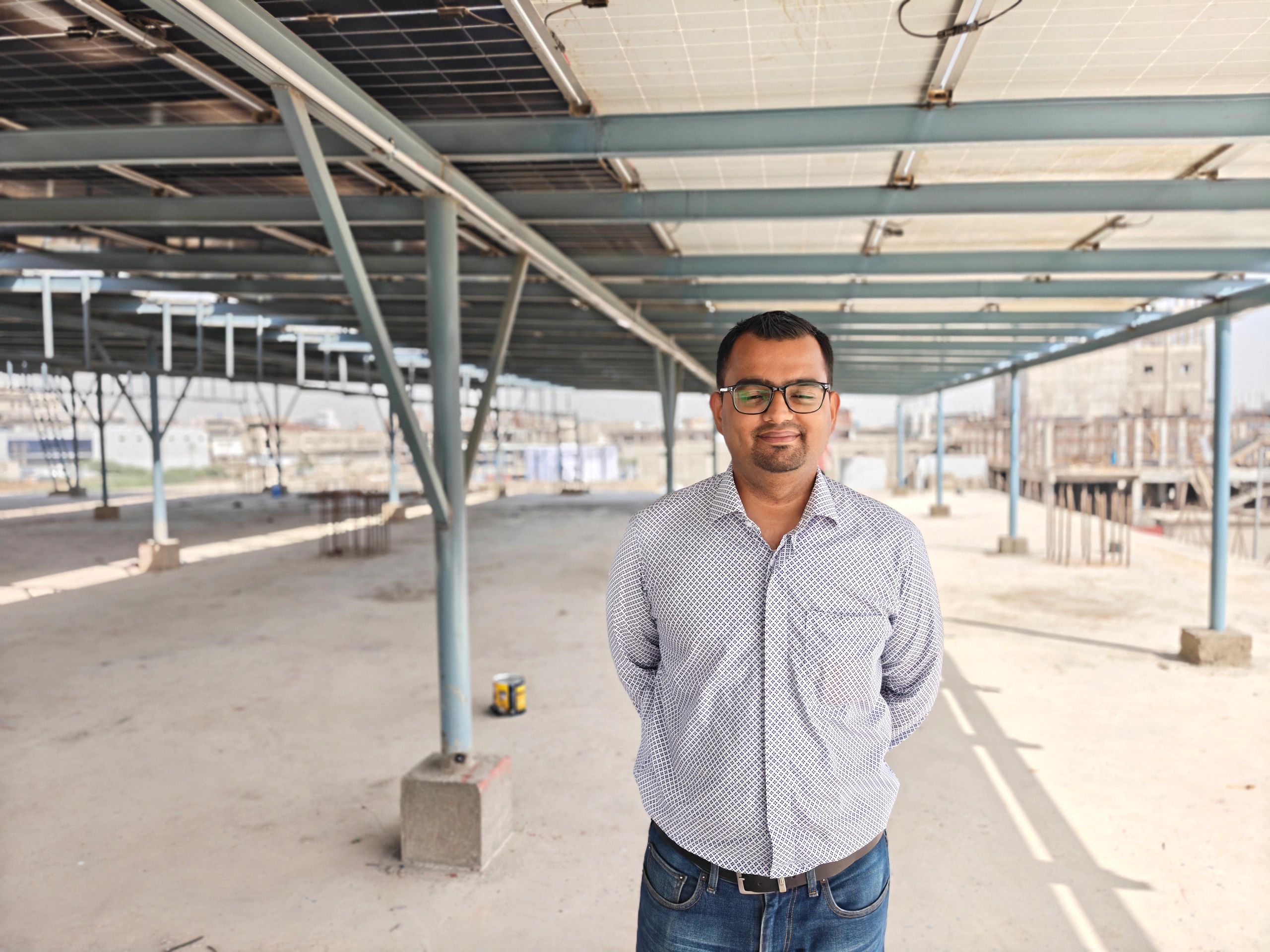 Man with glasses and folded hands in white shirt under metal canopy