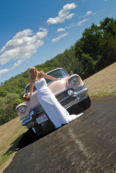 elegant bride with a classic car on a rural road on a bright sunny day