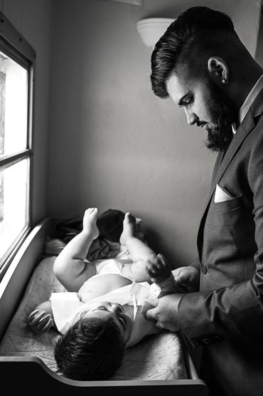 window-lit black and white photo of the groom changing his baby's diaper prior to the ceremony