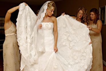 bridesmaids inspect the dress as they assist the bride