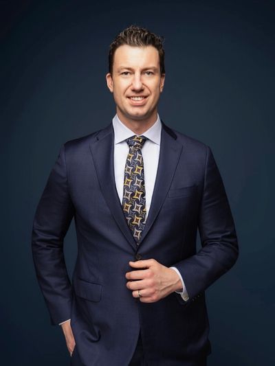 Man in navy suit with patterned tie smiling.