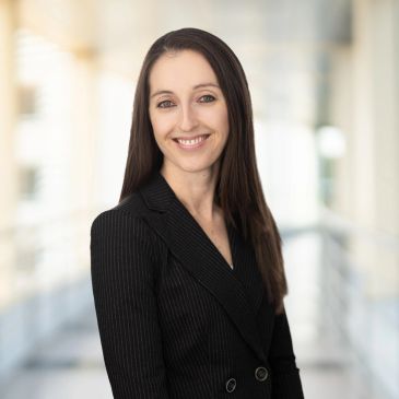 Smiling woman in black blazer posing indoors.