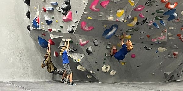 People climbing a manufacture rock wall at an indoor climbing gym.