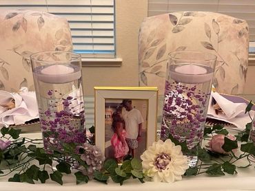 Table centerpiece with candles, flowers, and a framed photo between two chairs.