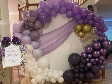 Decorative balloon arch in purple and white hues with a welcome sign for a bridal shower.