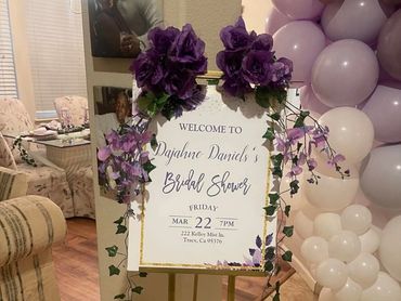 Welcome sign for Dajahne Daniel's bridal shower adorned with purple flowers and balloons.