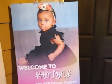 A baby girl in a black dress welcomes guests to her 1st birthday party.