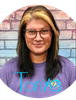 Woman with glasses smiling against a brick wall.