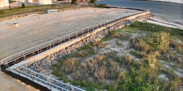 Coastal area with a fenced path and mixed vegetation near water.