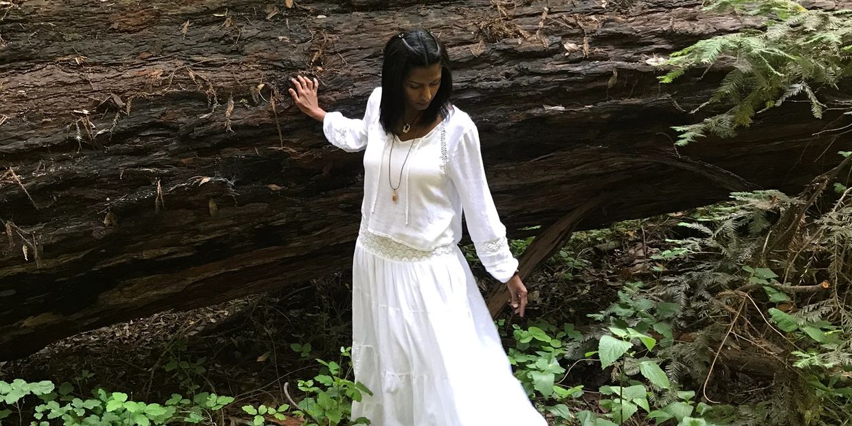 Galactic Charm wearing all white and standing by a fallen Redwood
