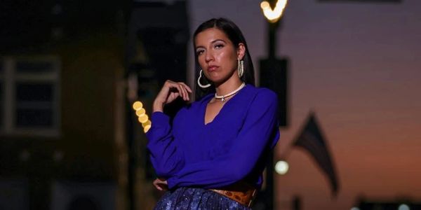 Woman in blue outfit posing confidently at dusk with city lights behind her.