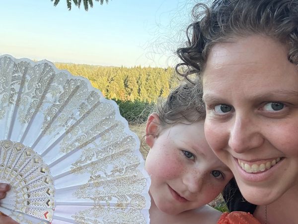 Smiling woman and child with a decorative fan outdoors in nature.