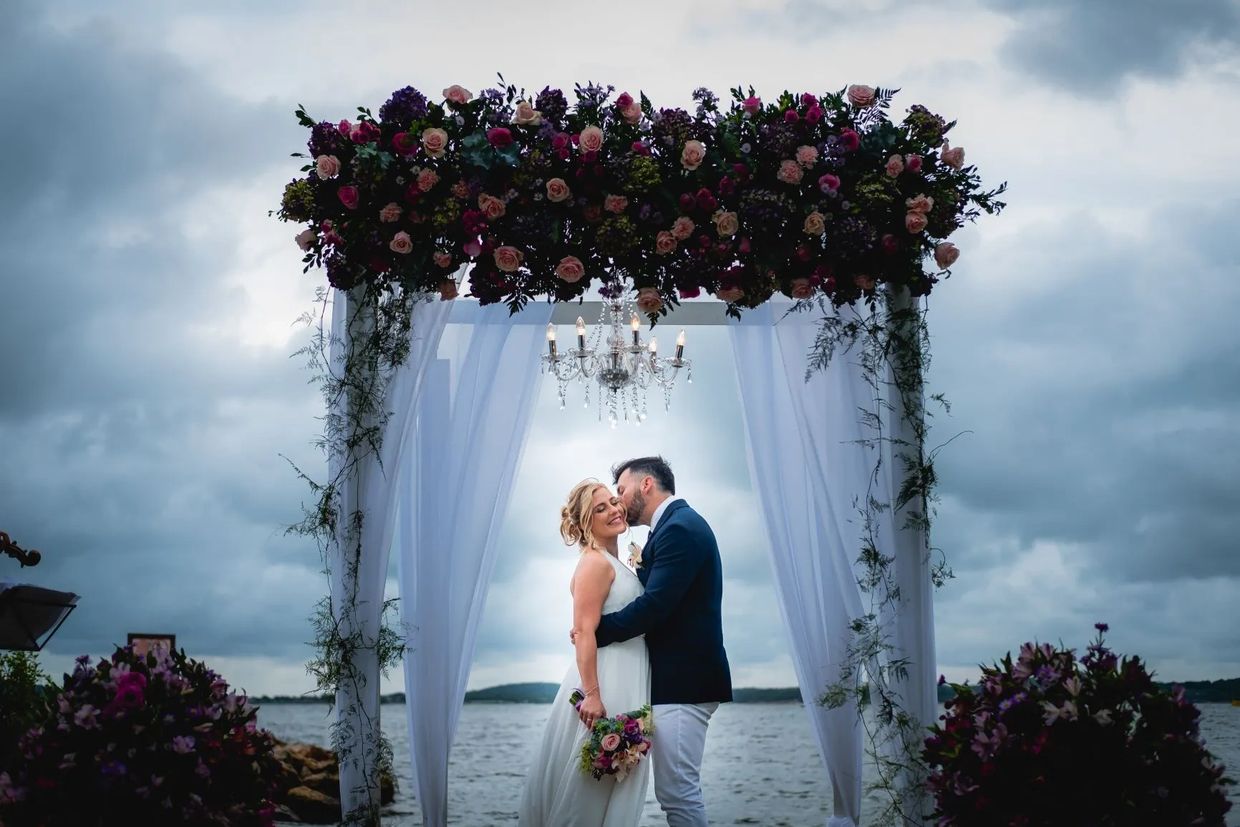 Una pareja de recién casados se besa tiernamente bajo un arco floral exquisito, 