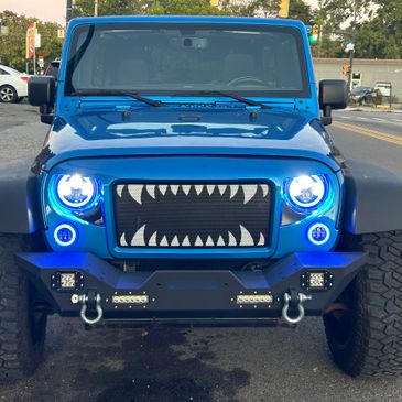 Blue Jeep with shark teeth grill and glowing blue headlights.