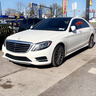 White Mercedes-Benz sedan parked on a sunny street near a gas station.