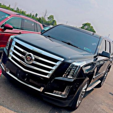 Black Cadillac SUV parked outdoors beside a red car.
