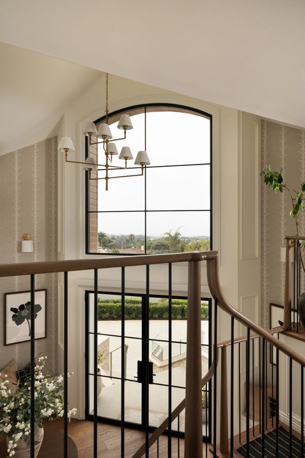 Elegant staircase with large arched window and classic chandelier.