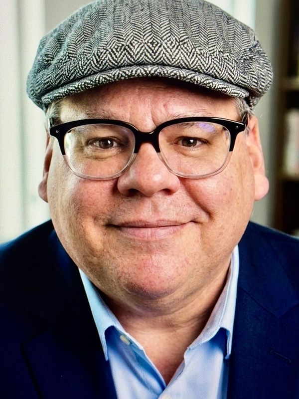 Smiling man wearing glasses and a patterned flat cap.
