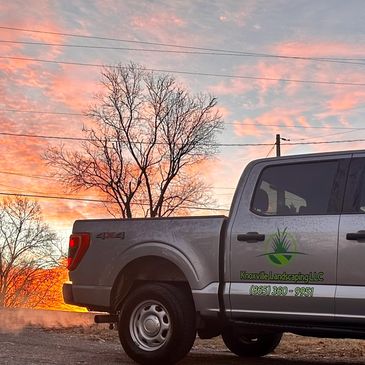 Silver truck with Knoxville Landscaping logo and pink sky sunrise in background 